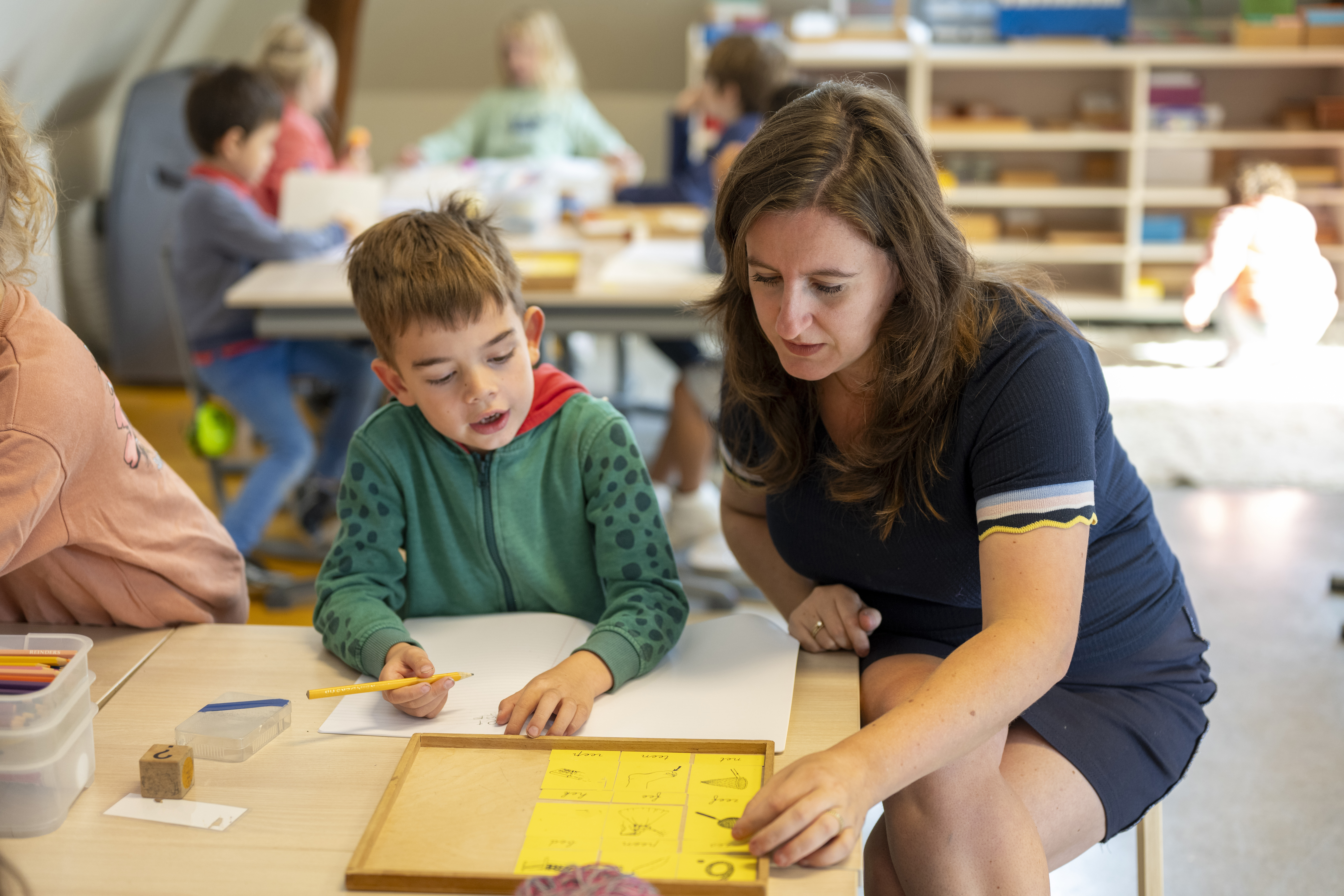 A teacher engaging with a young student during a classroom activity.