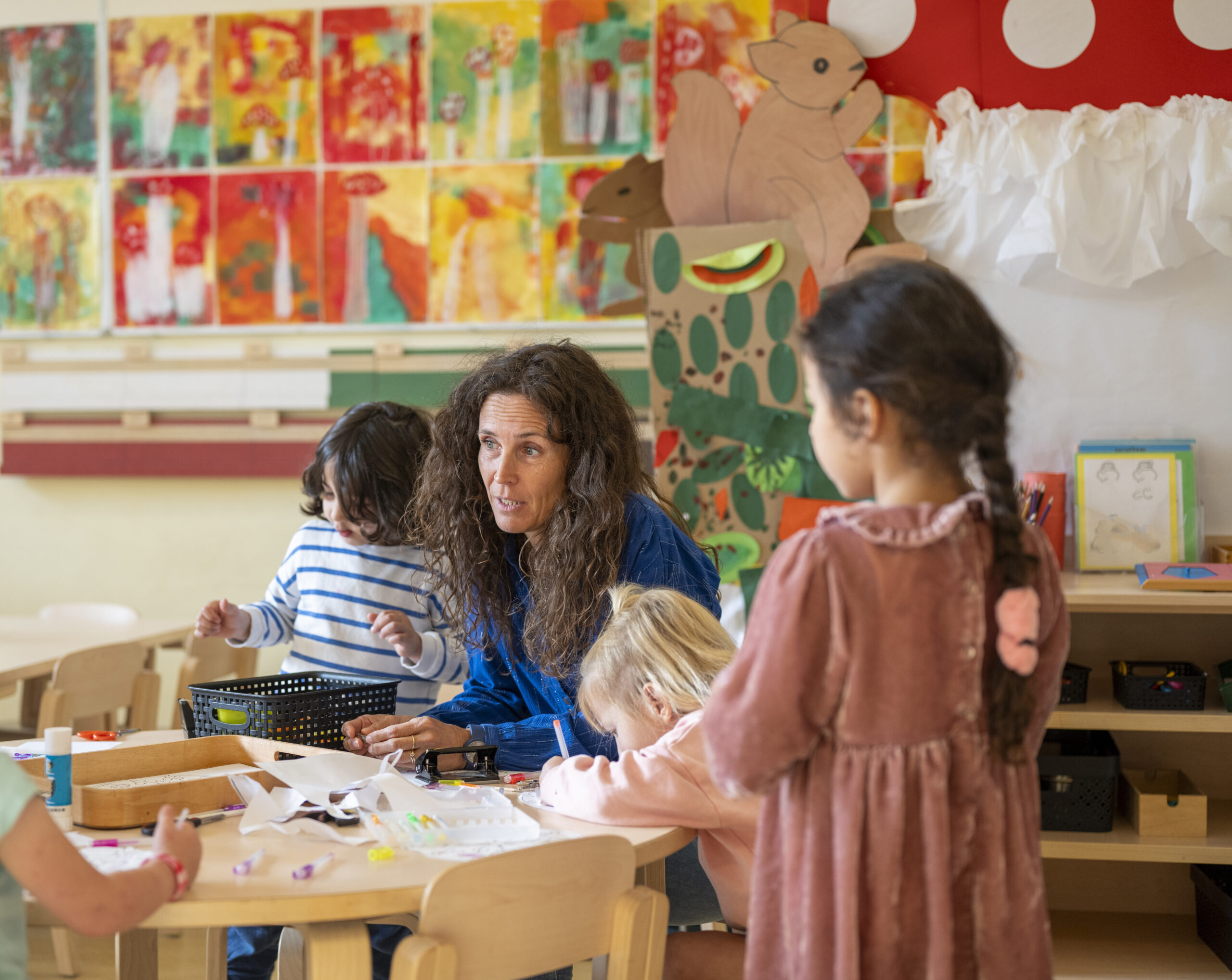 Happy encouraging teacher speaking to her class, young group of children listening to their lesson